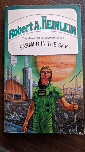 Trade paperback edition of Robert A. Heinlein's Farmer in the Sky. A young man with a very serious face and ridiculous hair stands on a the rocky surface of Ganymede, with Jupiter hanging large in the sky. He wears a green jumpsuit with special gadgets attached, partially hooded, and sporting aviator sunglasses while looking to the sky with a scowl. He holds onto on end of a metallic, hi-tech, rod-like farming implement, he other end on the ground. In the background is something that looks like a barn with a mainframe computer visible through the barn door and a satellite dish mounted from the roof. Beside the barn is something that looks like a cross between a grain silo and a rocket silo, with lots of antennae protruding from it.